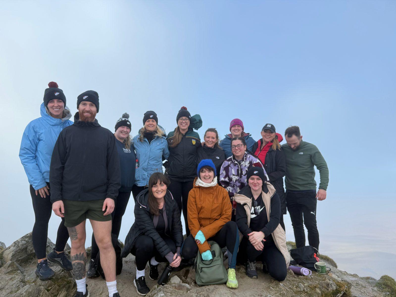 Intensity Fitness members and coaches posing together at a misty mountain summit in hats and jackets